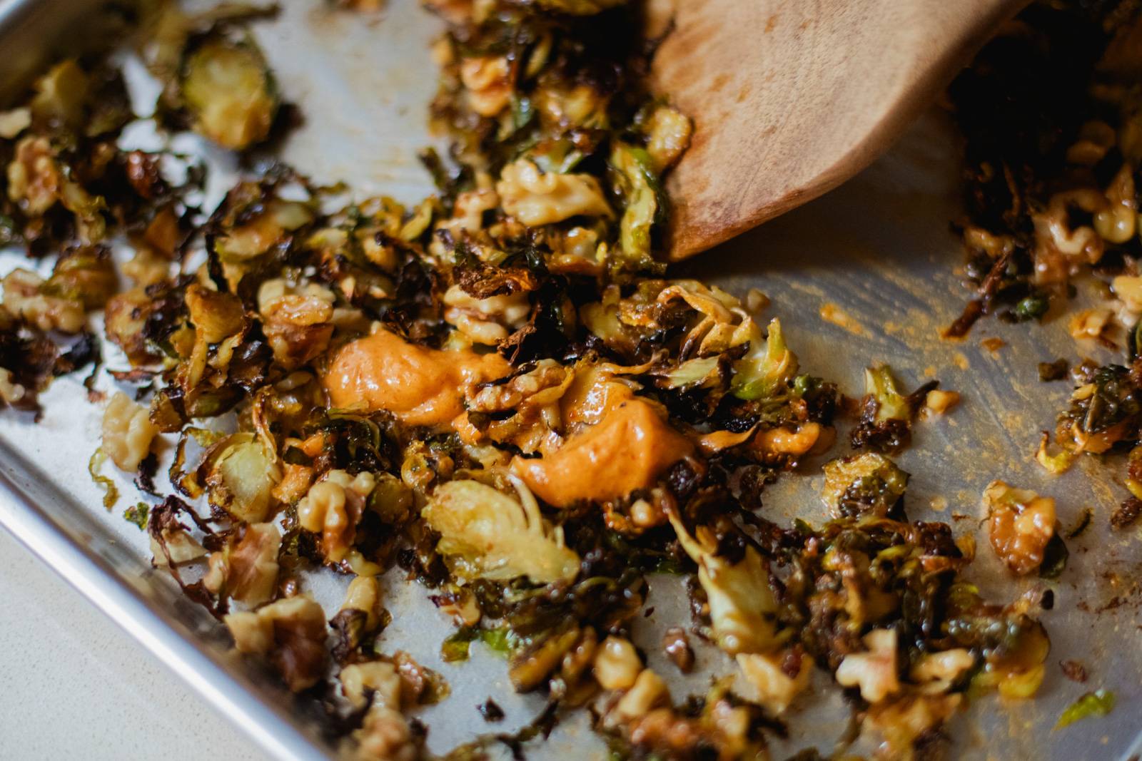 Tossing roasted brussels sprouts with gochujang butter on a sheet pan.