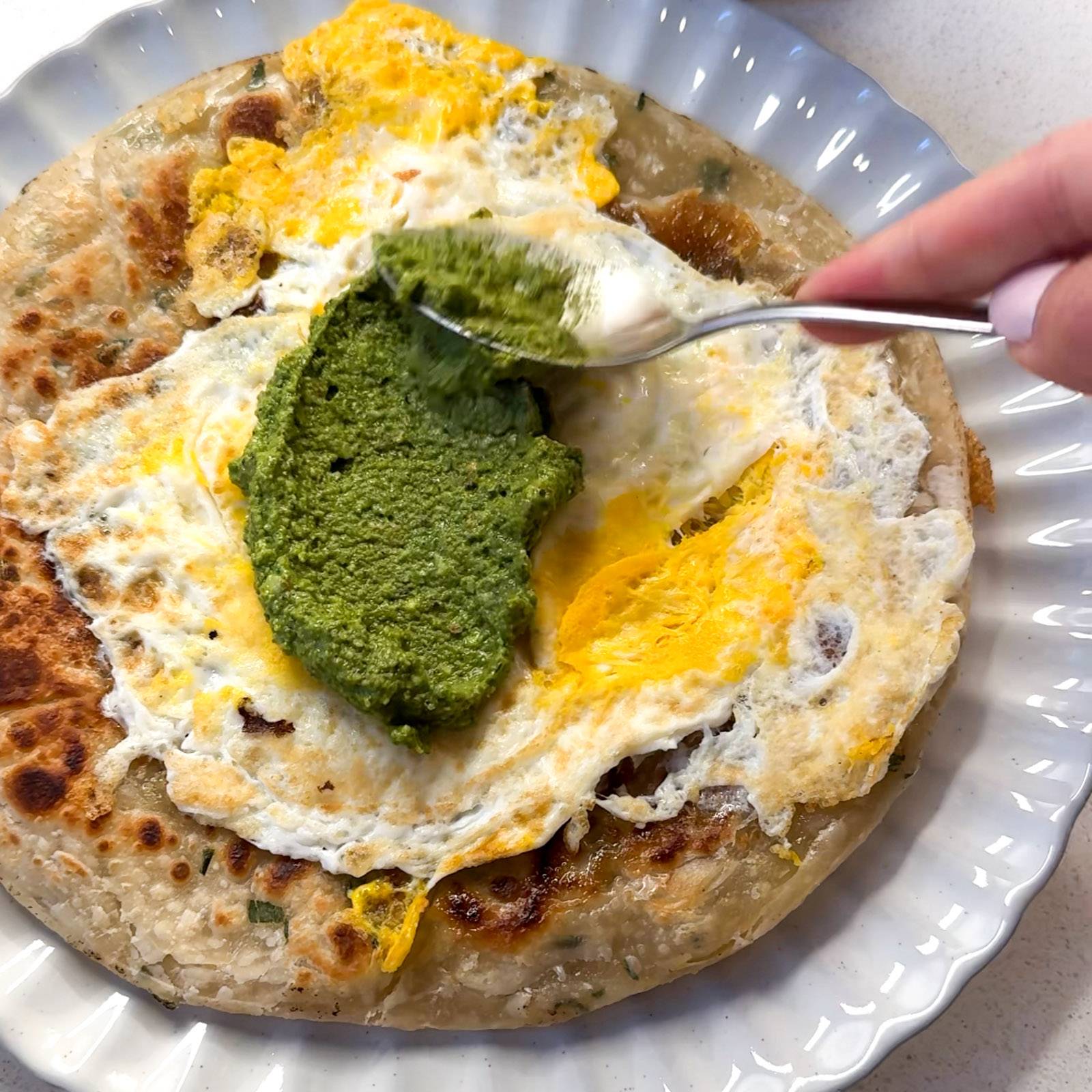 Spreading cilantro pesto on a scallion pancake with egg.