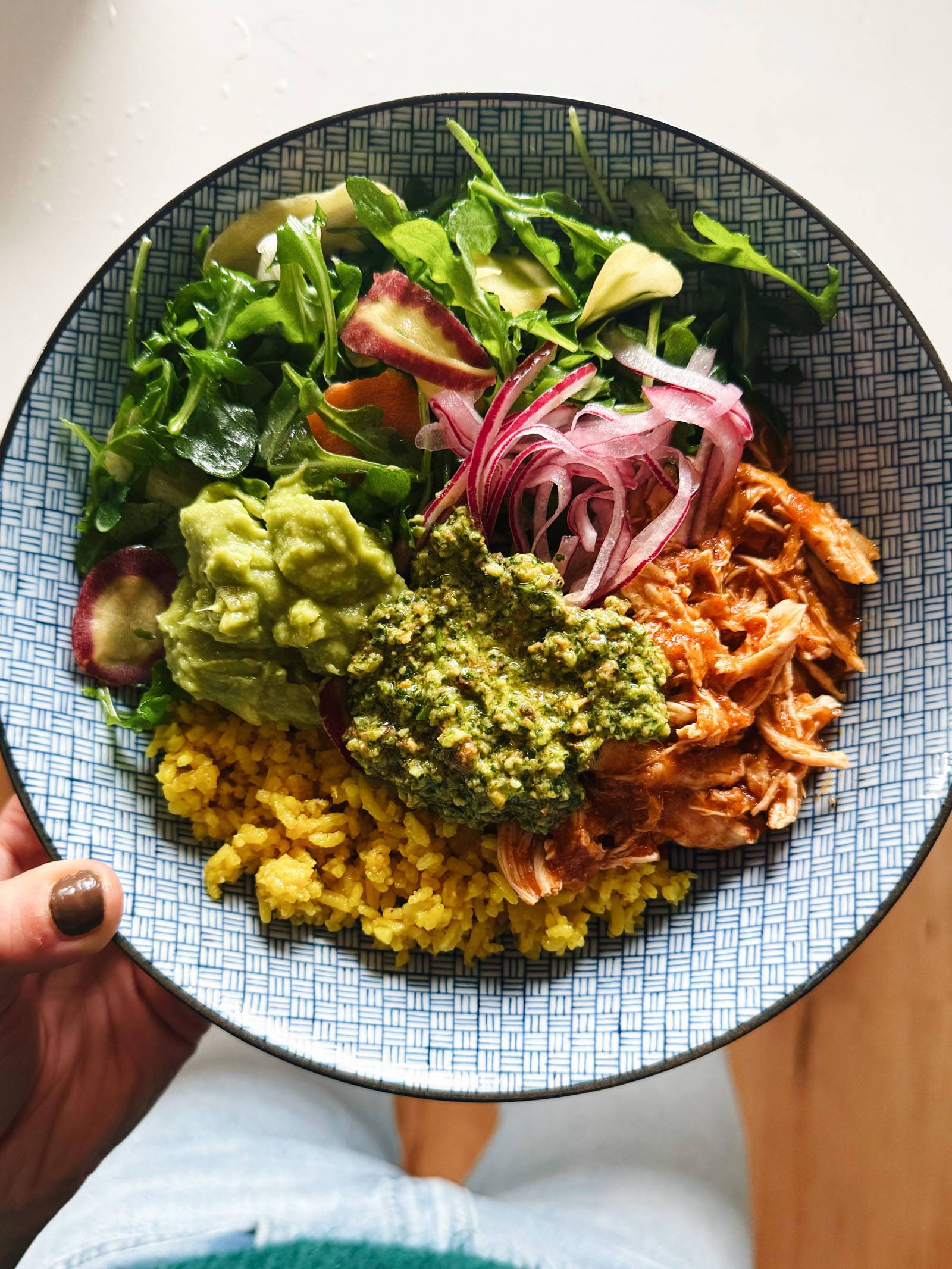 Chicken bowl with yellow rice, greens, and cilantro pesto on top.