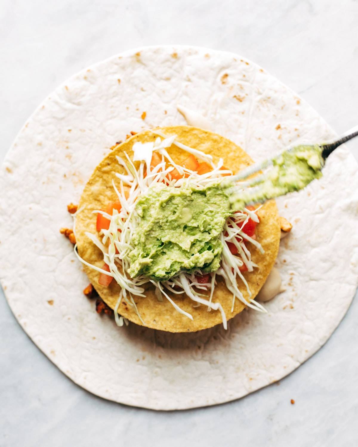 Adding guacamole to vegan crunchwrap supreme.