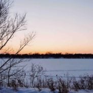 A winter scene with snow covering an empty field beneath a sky tinged with orange.