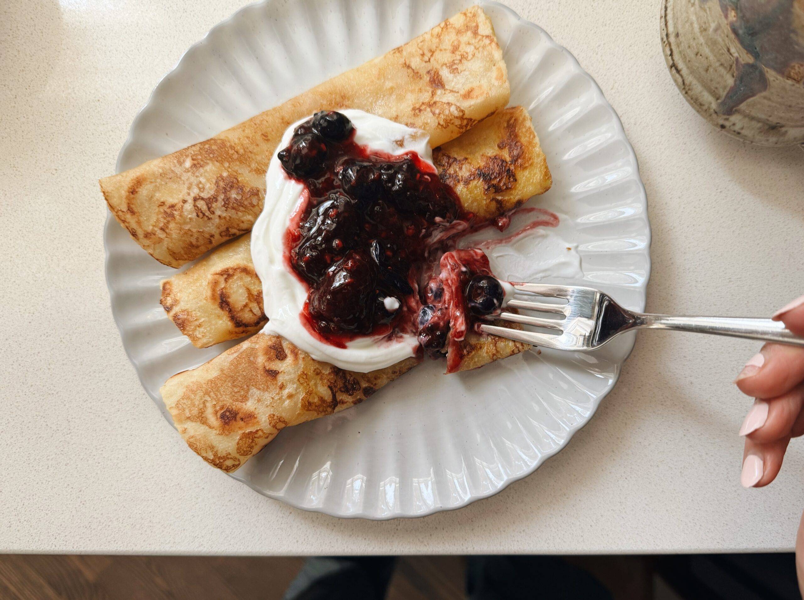 French toast crepes on a plate topped with yogurt and blueberry sauce.