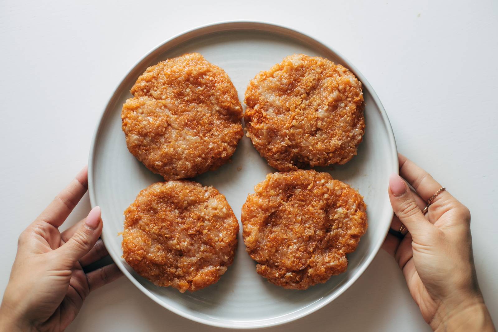 Four raw chicken burgers on a plate