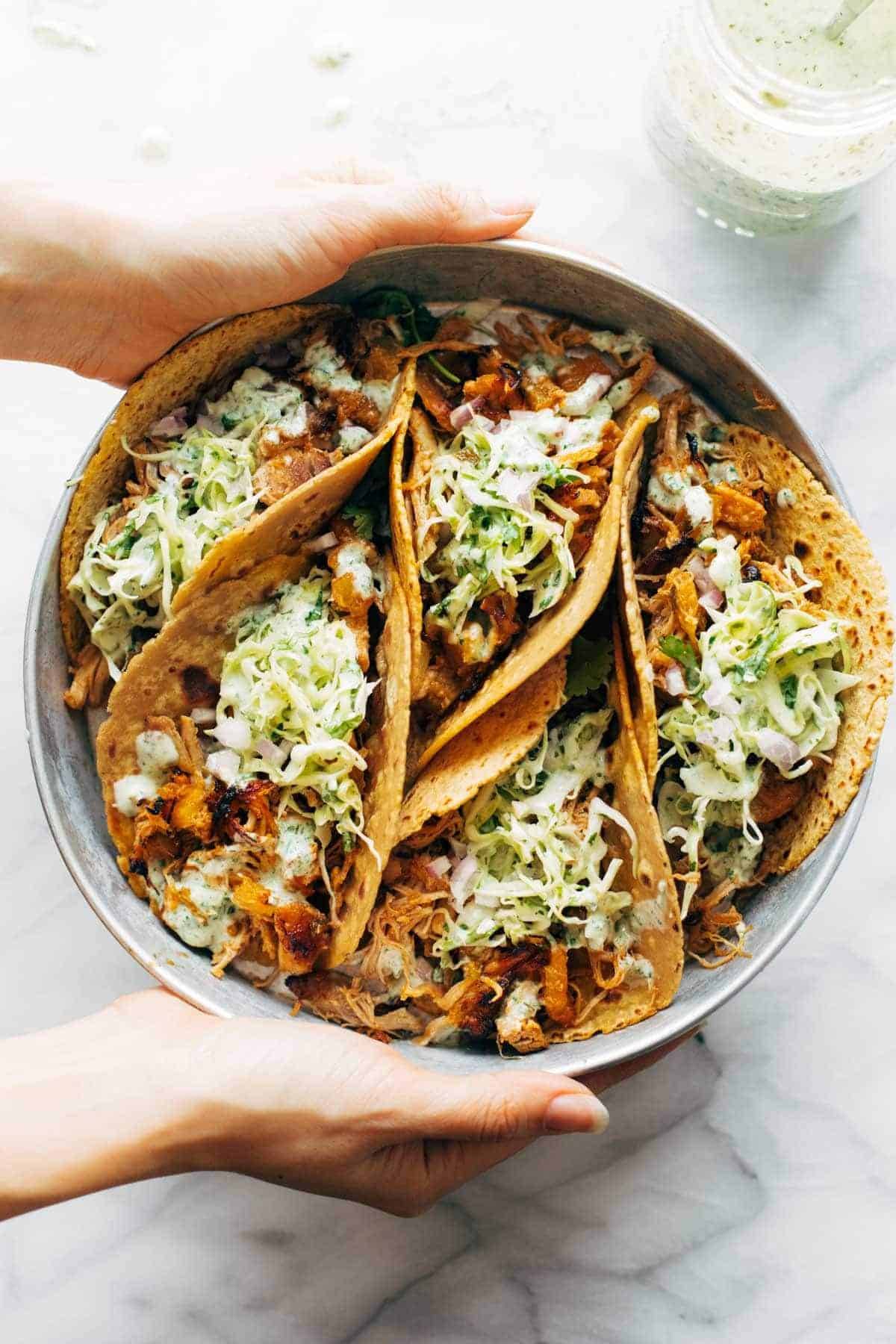 Hawaiian Chicken Tacos on a plate. White hands are holding the plate. 