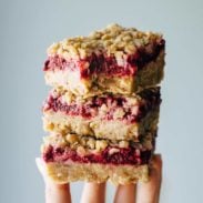 Raspberry crumble bars stacked with a hand.