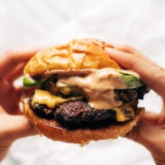 Hands holding a juicy smash burger with sauce.