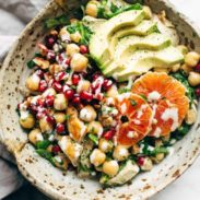 Spa salad in a bowl topped with chicken, avocado, and oranges.