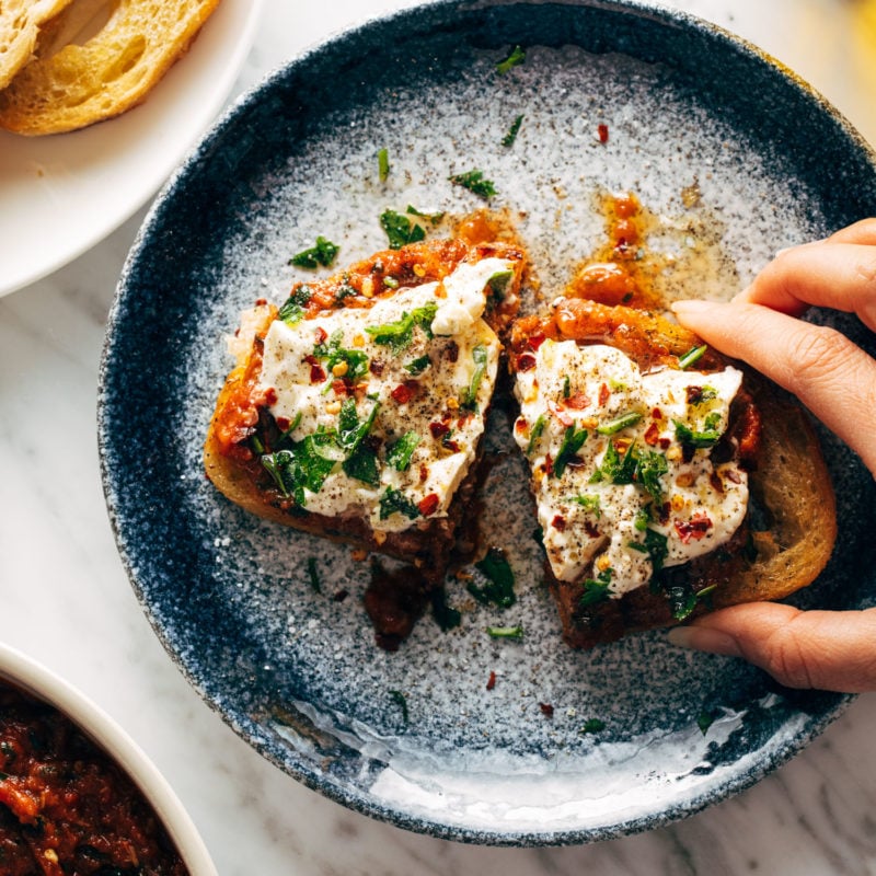 White hand grabbing Zaalouk toast on a plate